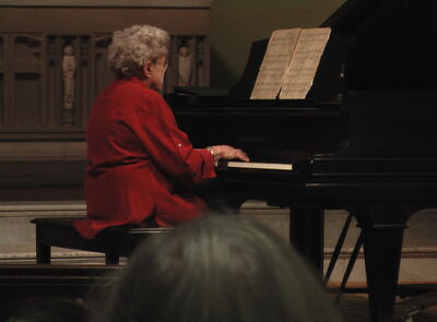 Keywords: old lady,piano,musician,pianist,red top,grey hair,facing away,score,playing