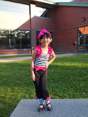 Keywords: smiling girl,pink bows,striped top,black pants,school,outdoors,grass