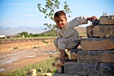 Keywords: boy,child,kid,stones,bricks,outdoors,smiling,kneeling,white outfit,tree