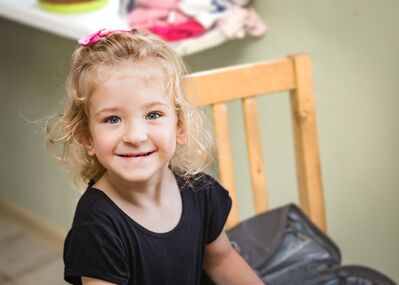 Keywords: portrait,girl,smiling,blonde,pink ribbon in hair,chair,black top,shirt,case