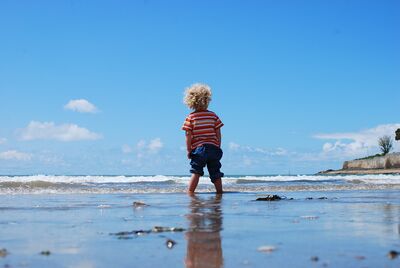 Keywords: portrait,child,kid,children,orange stripes,blue pants,curly blonde hair,wading,seashore,ocean,beach,sky,back view