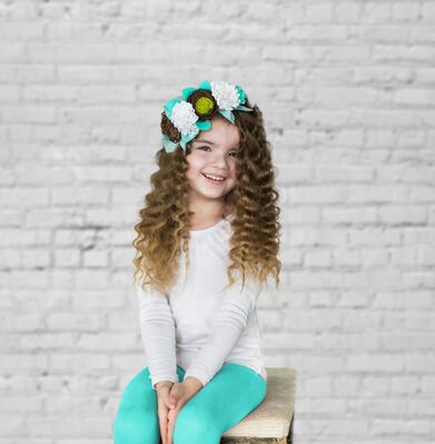 Keywords: girl,curly hair,white top,aqua pants,blue,green,hat,matching outfit,seated on chair,white bricks beind