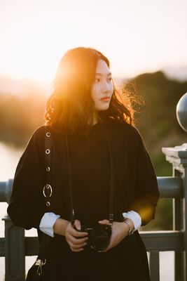 Keywords: girl,woman,youth,young,photographer,camera,sunlight,black coat,jacket,fence,asian,white cuffs,hands