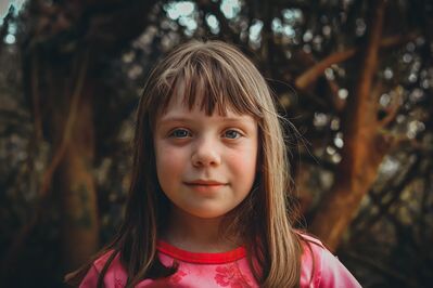 Keywords: girl,kid,child,red print top,tree trunks in background,bangs,brown hair