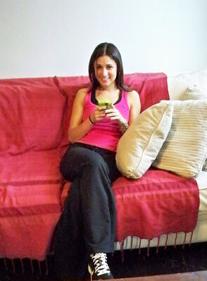 Keywords: girl on red sofa,throw,couch,cell phone,green,pink top,black slacks,pants,pillows,yellow