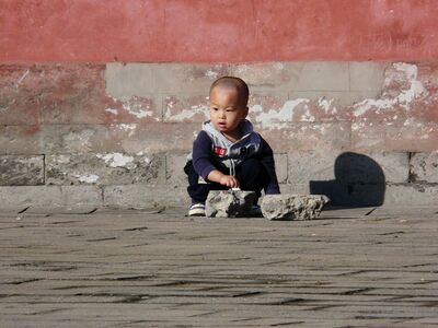 Keywords: child,boy,kid,sitting,outdoors,rocks,wall,blue jacket,black pants,asian