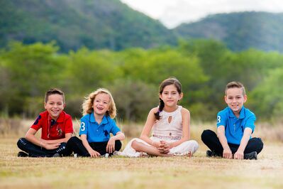 Keywords: portrait,four,children,kids,sitting,ground,grass,dry,two,blue shirts,red,white dress,black pants,green trees