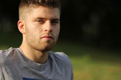 Keywords: young man,outdoors,green grass,grey shirt,stubble,facial hair