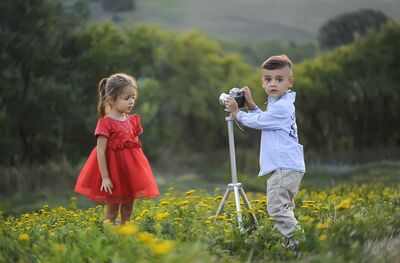 Keywords: children,child,girl,boy,camera,field,yellow flowers,trees,red dress,white shirt and pants