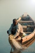 Man_Sitting_on_Wooden_Fishing_Boat_on_Lake.jpg